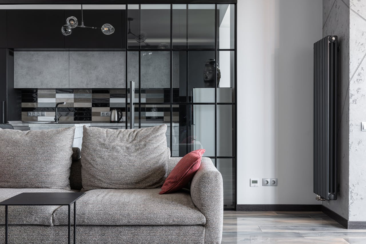 Contemporary living space featuring a stylish gray sofa, red cushion, and a view into a modern kitchen.